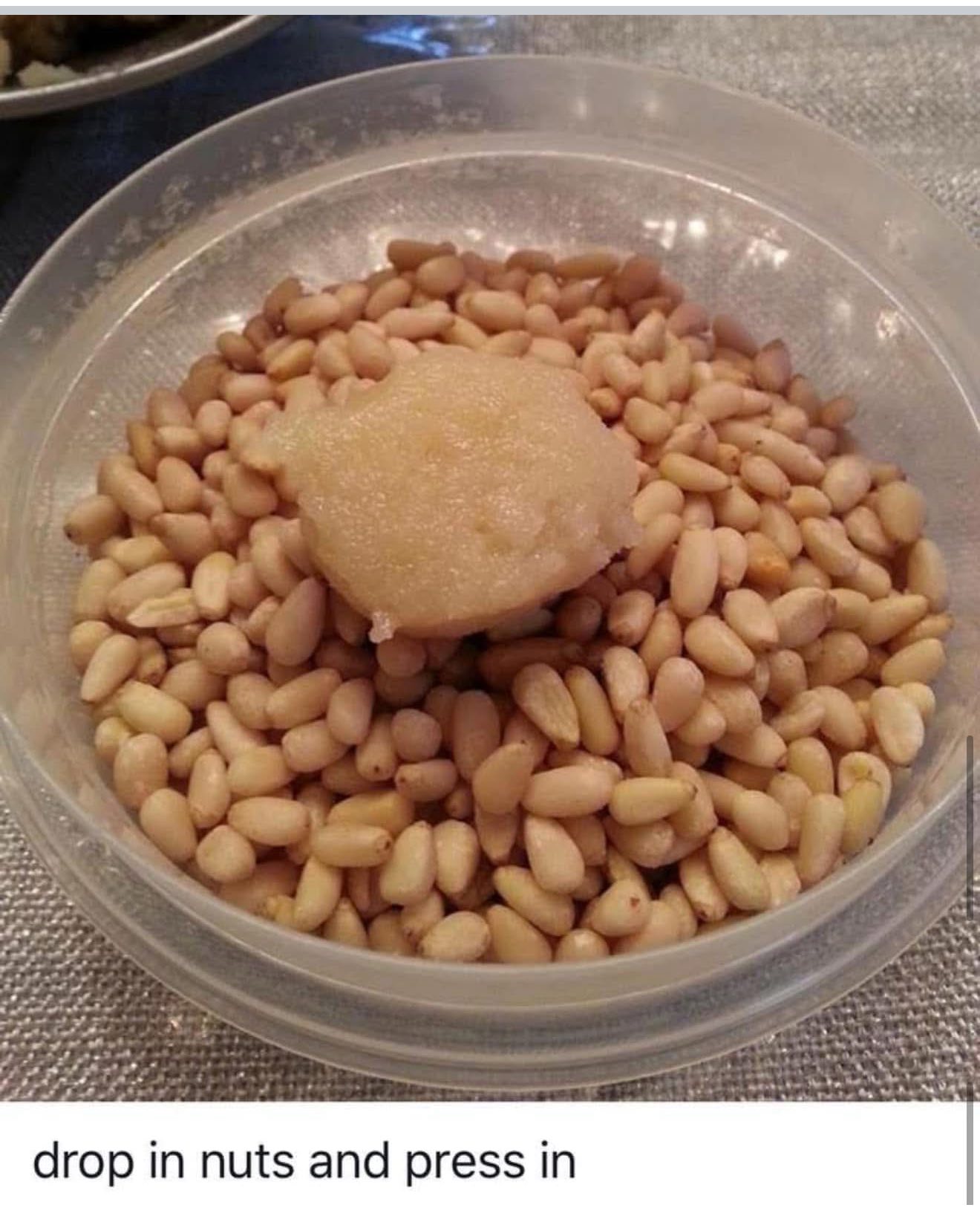 A scoop of raw almond dough dropped into a bowl of pine nuts ready to be rolled