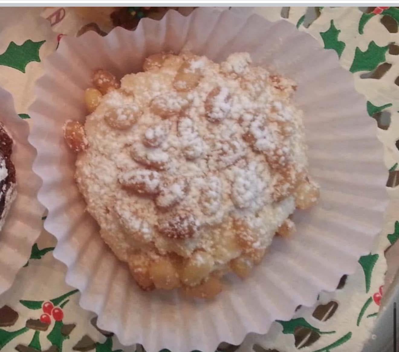Close up of a single finished Pignoli cookie dusted with powdered sugar in a paper liner