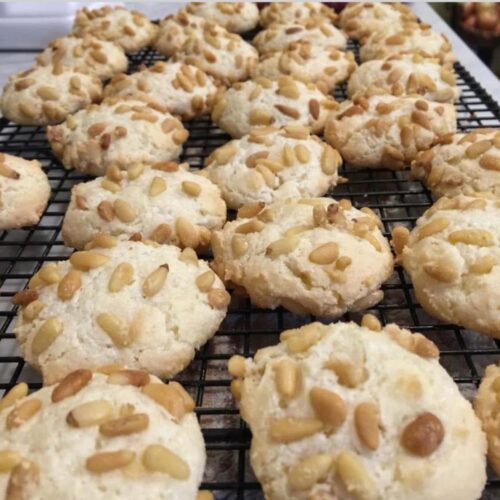 Wire rack filled with golden brown Pignoli cookies covered in toasted pine nuts