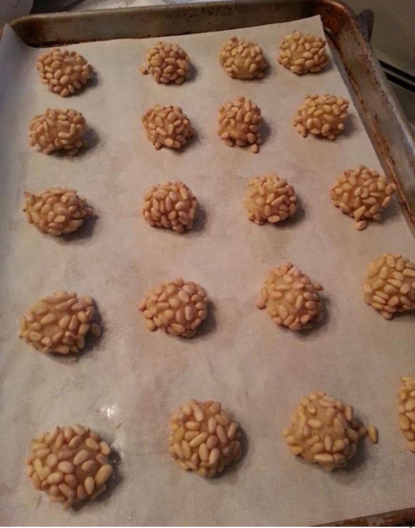 Raw Pignoli cookies lined up on a parchment covered baking sheet