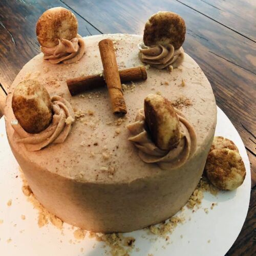 A beautiful three-layer snickerdoodle cake frosted with cinnamon buttercream, garnished with mini snickerdoodle cookies and whole cinnamon sticks.