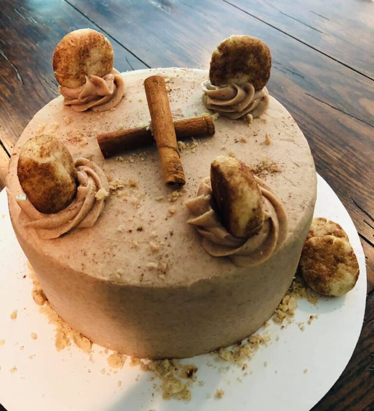 A beautiful three-layer snickerdoodle cake frosted with cinnamon buttercream, garnished with mini snickerdoodle cookies and whole cinnamon sticks.