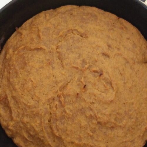 A freshly baked, golden brown homemade sweet potato bread in a black cast iron skillet.