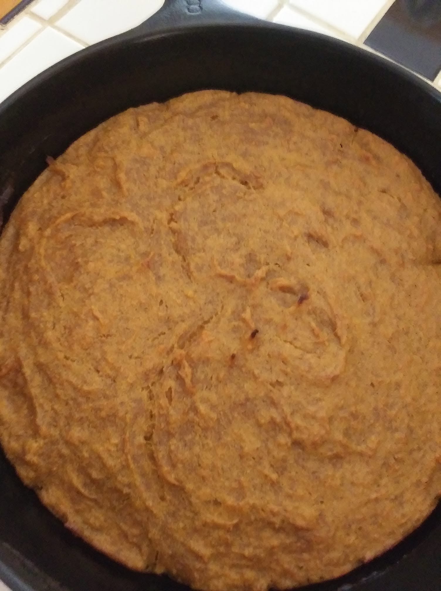 A freshly baked, golden brown homemade sweet potato bread in a black cast iron skillet.