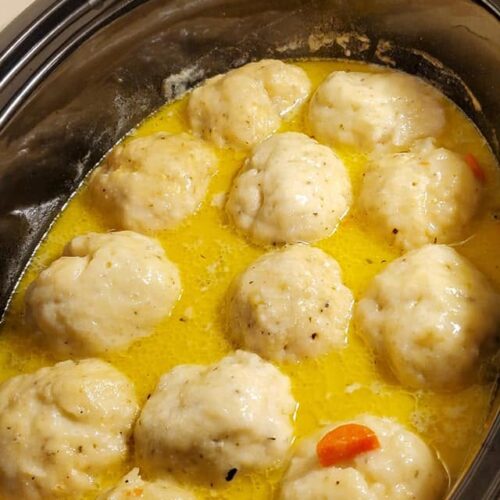 Large, fluffy homemade dumplings simmering in a rich, golden chicken broth in a slow cooker.