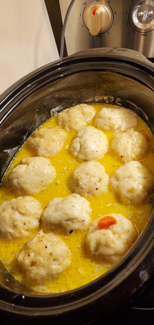 Large, fluffy homemade dumplings simmering in a rich, golden chicken broth in a slow cooker.