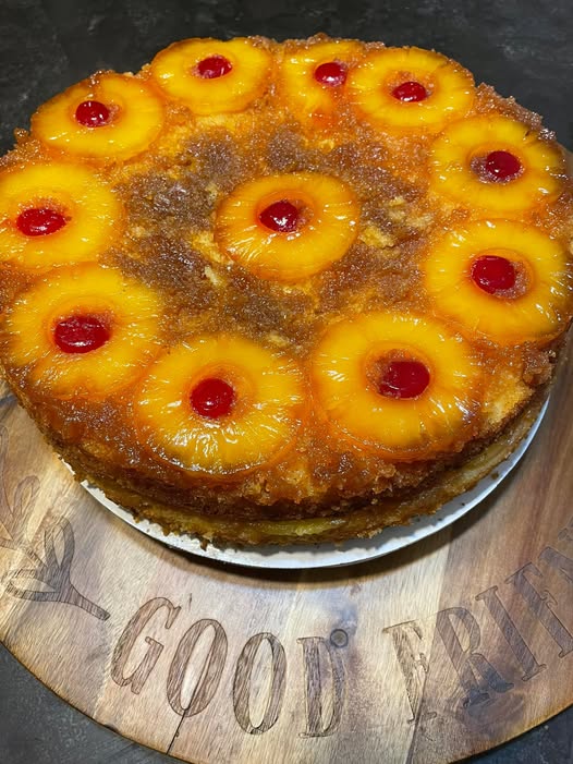 A beautiful two-layer pineapple upside-down cake resting on a wooden board, topped with caramelized pineapple rings and bright red maraschino cherries.
