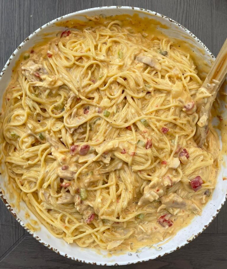 A large rustic bowl overflowing with creamy, cheesy chicken spaghetti speckled with diced tomatoes and green peppers.