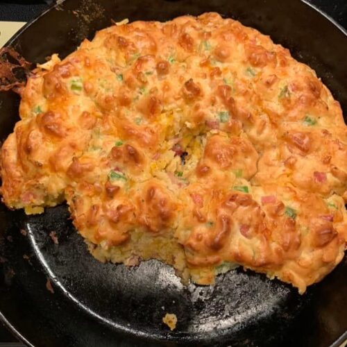 A golden brown, freshly baked ham and cheese drop biscuit bread in a black cast iron skillet.