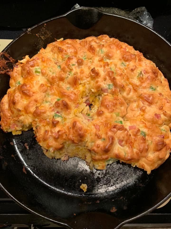 A golden brown, freshly baked ham and cheese drop biscuit bread in a black cast iron skillet.