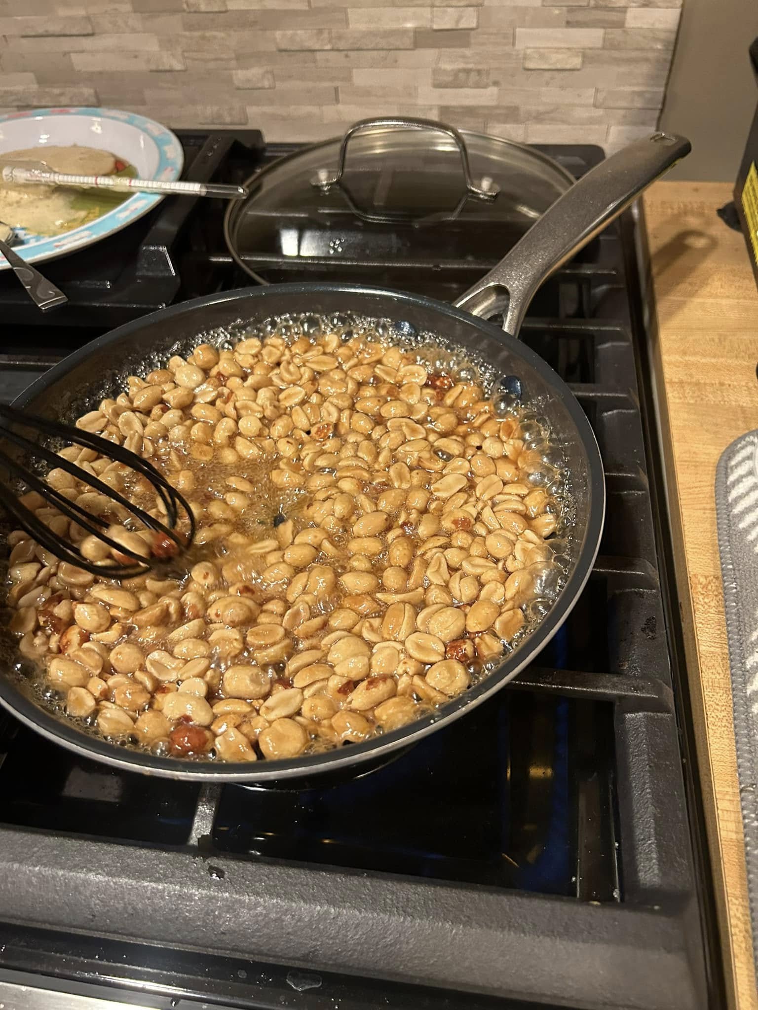 A nonstick skillet on a gas stove filled with peanuts bubbling rapidly in a thin, watery maple syrup glaze.