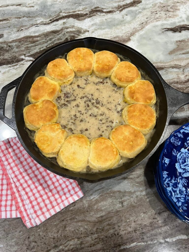 A black cast iron skillet filled with creamy sausage gravy in the center, surrounded by a ring of perfectly golden-brown baked biscuits.