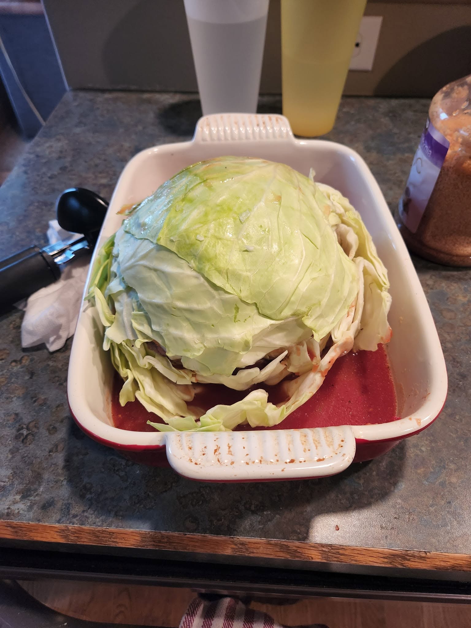 Raw meatballs packed inside a hollowed-out cabbage bowl, generously covered in a rich red tomato sauce before baking.