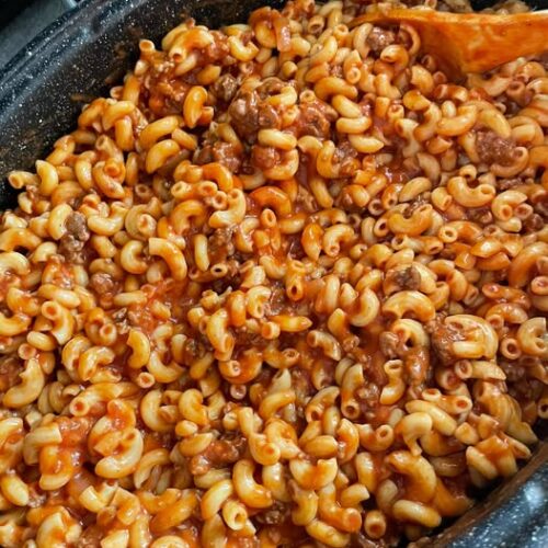 A large speckled roasting pot filled with hearty Northern-style goulash featuring elbow macaroni, ground beef, and a rich tomato sauce.