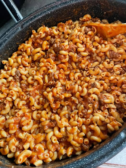 A large speckled roasting pot filled with hearty Northern-style goulash featuring elbow macaroni, ground beef, and a rich tomato sauce.
