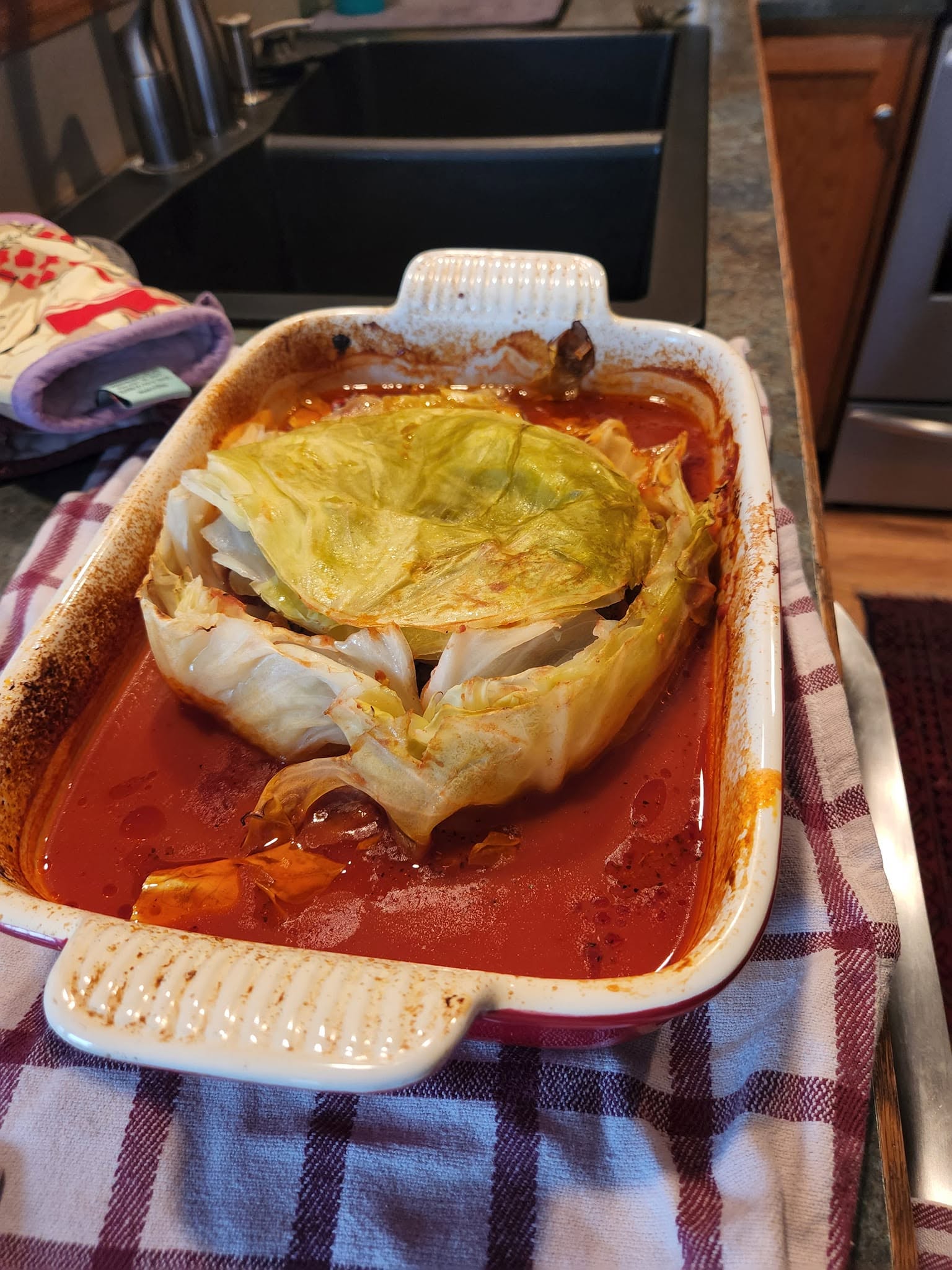 A fully baked cabbage bowl sitting in a bubbling red tomato sauce inside a casserole dish, fresh out of the oven with the lid slightly askew.