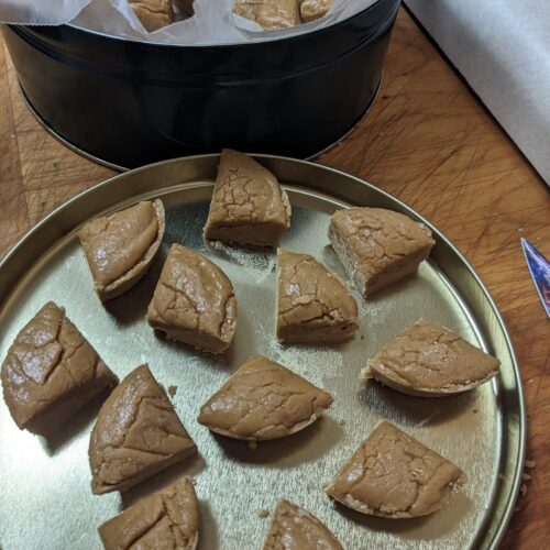 Pieces of light brown Sucre à la Crème maple fudge cut into triangular wedges, displayed in a metal tin.