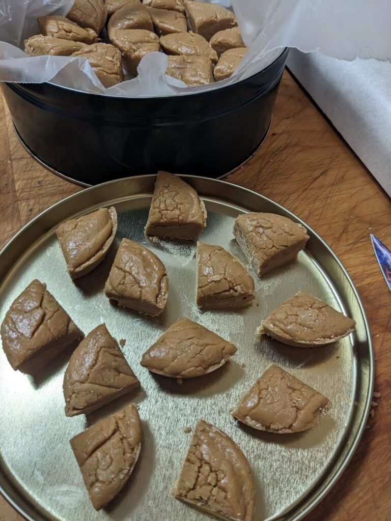 Pieces of light brown Sucre à la Crème maple fudge cut into triangular wedges, displayed in a metal tin.