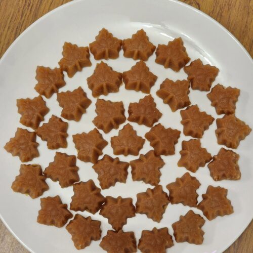 A white plate filled with beautiful, perfectly formed maple leaf-shaped candies made from pure maple syrup.