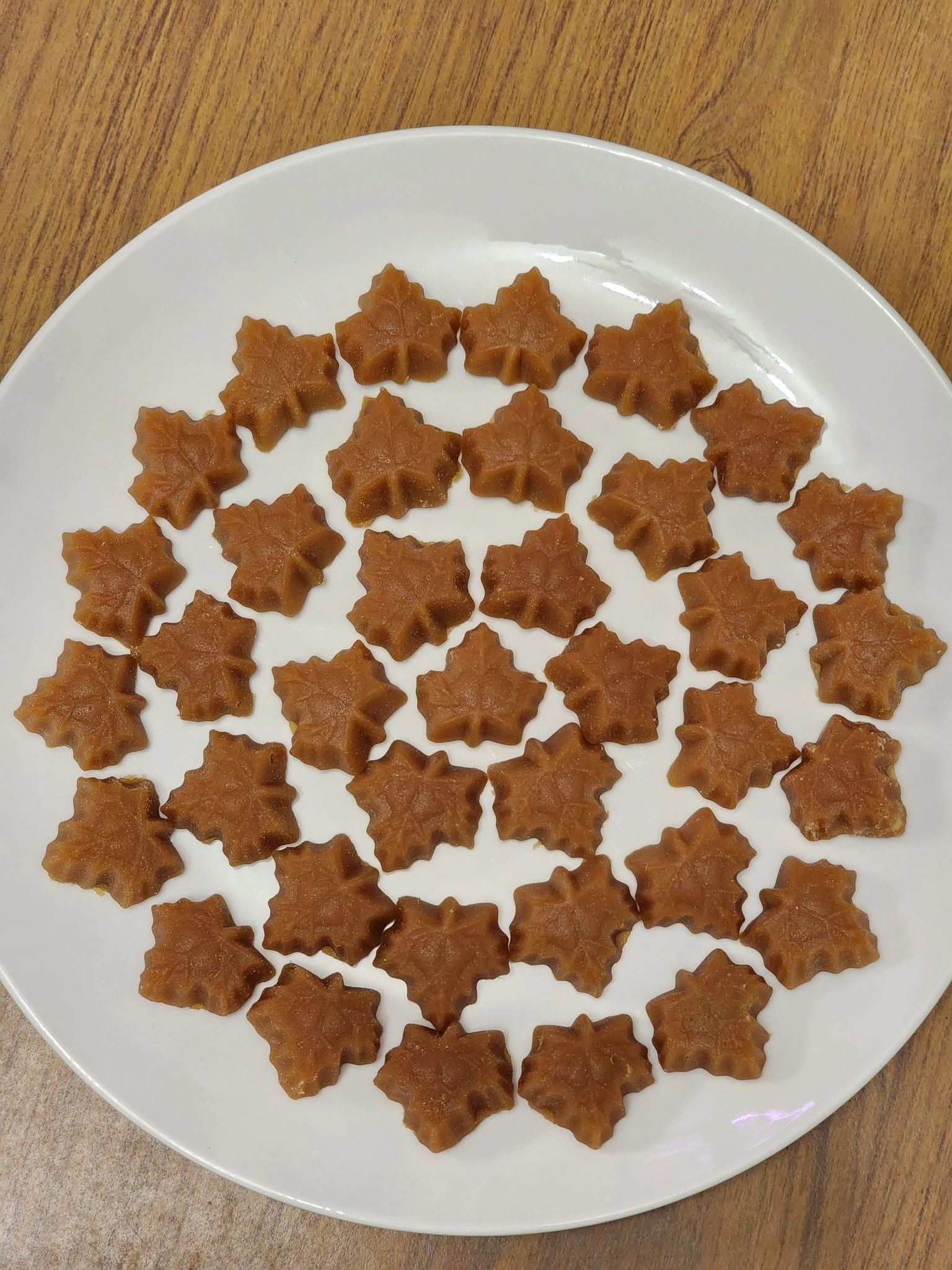 A white plate filled with beautiful, perfectly formed maple leaf-shaped candies made from pure maple syrup.
