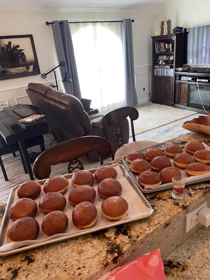 Freshly fried golden brown Polish pączki donuts cooling on parchment-lined baking trays before glazing.