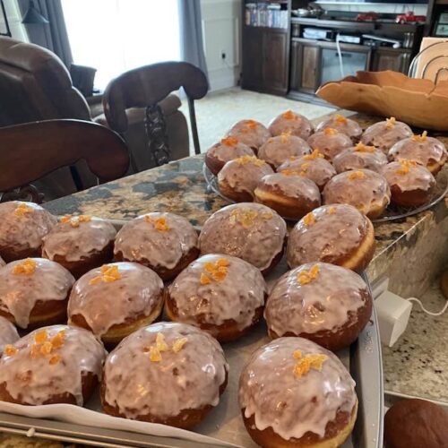 Homemade Polish pączki donuts covered with white sugar glaze and candied orange peel, arranged on baking trays.