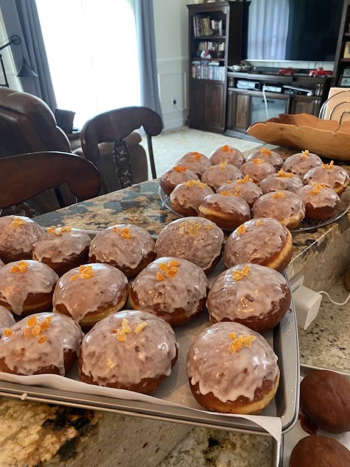 Homemade Polish pączki donuts covered with white sugar glaze and candied orange peel, arranged on baking trays.