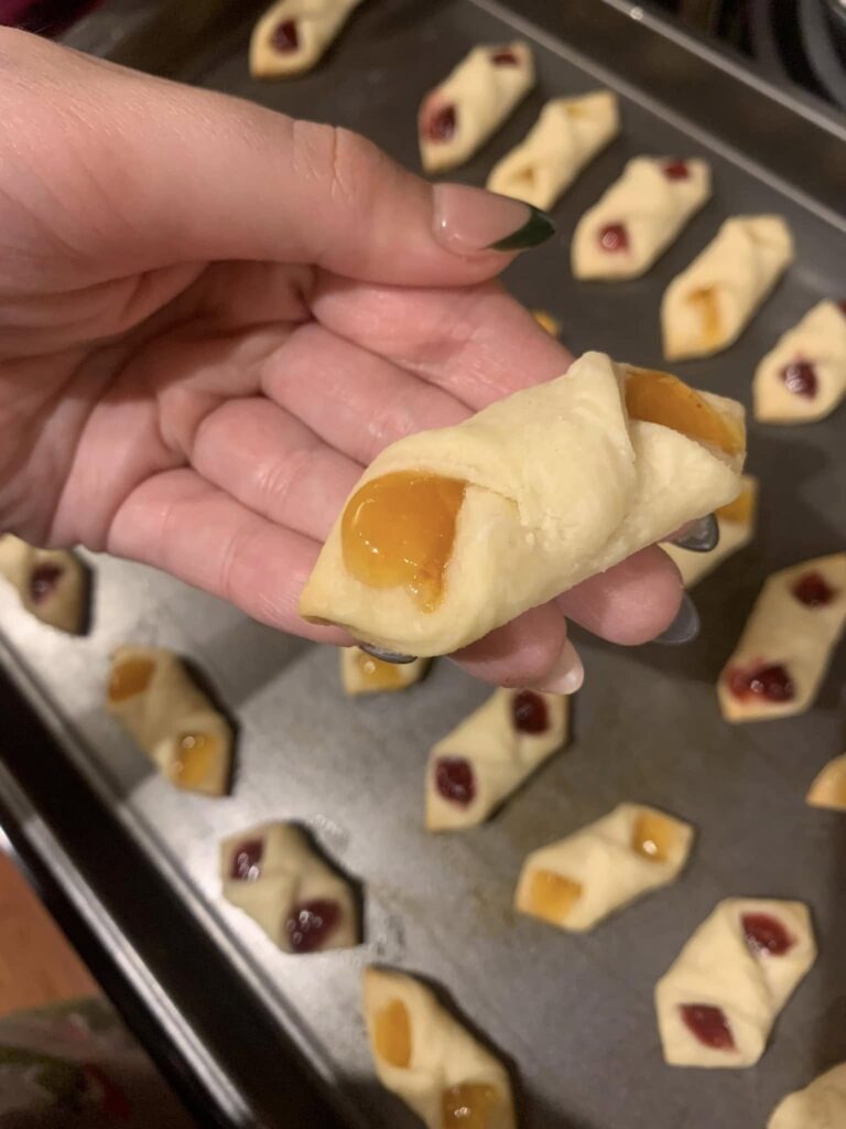 Homemade Polish Kołaczki cookies filled with apricot and raspberry preserves arranged on a baking sheet.