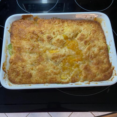 A glass baking dish filled with bubbly, golden brown peach cobbler dump cake featuring a buttery crust over sweet fruit filling.