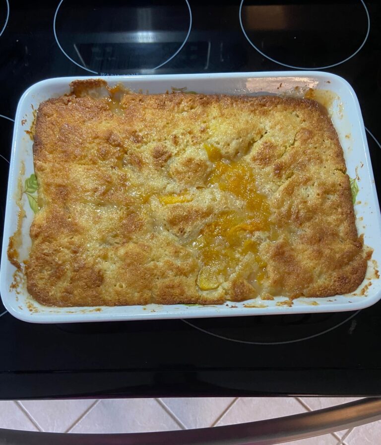 A glass baking dish filled with bubbly, golden brown peach cobbler dump cake featuring a buttery crust over sweet fruit filling.