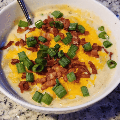 A large, rustic wooden bowl filled with rich, creamy potato soup topped with crisp bacon and green onions, with the full slow cooker pot resting on the counter in the background.