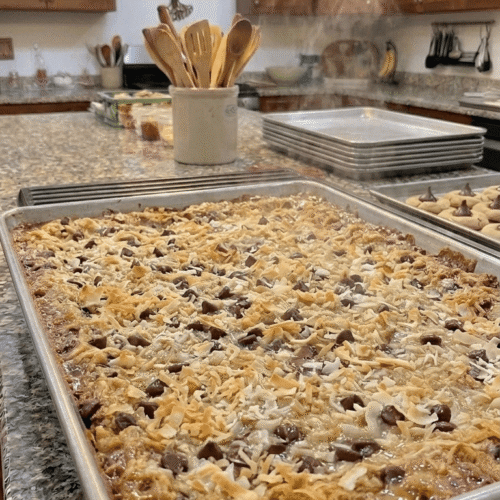 A stack of chewy 7-layer magic cookie bars showing a thick graham cracker crust, gooey chocolate chips, butterscotch, pecans, and perfectly toasted coconut.
