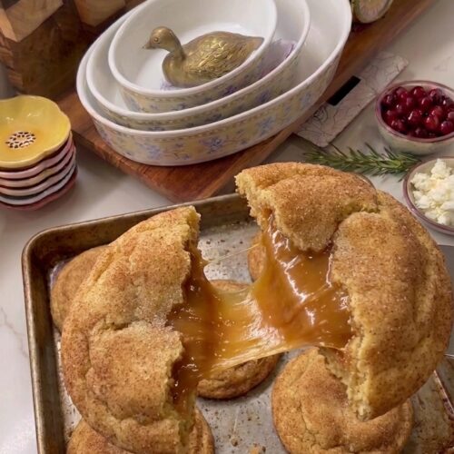 Soft caramel stuffed snickerdoodle cookies coated in cinnamon sugar, with one cookie broken open to reveal a gooey caramel center.