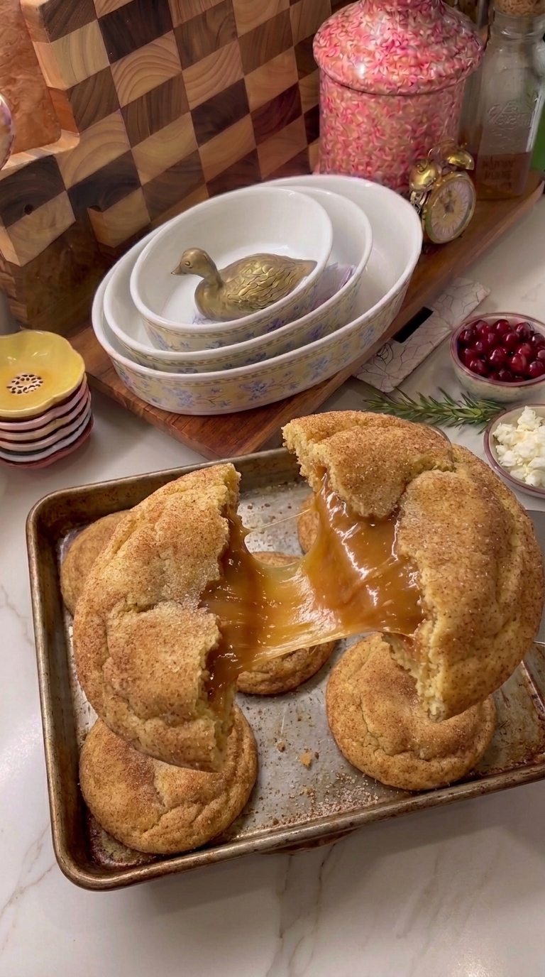 Soft caramel stuffed snickerdoodle cookies coated in cinnamon sugar, with one cookie broken open to reveal a gooey caramel center.