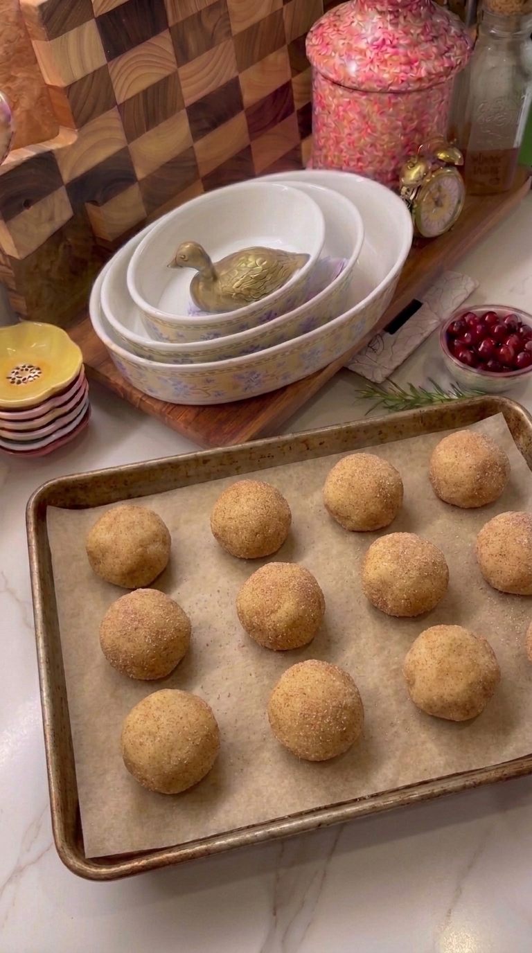 Unbaked caramel stuffed snickerdoodle cookie dough balls coated in cinnamon sugar and arranged on a parchment-lined baking sheet.