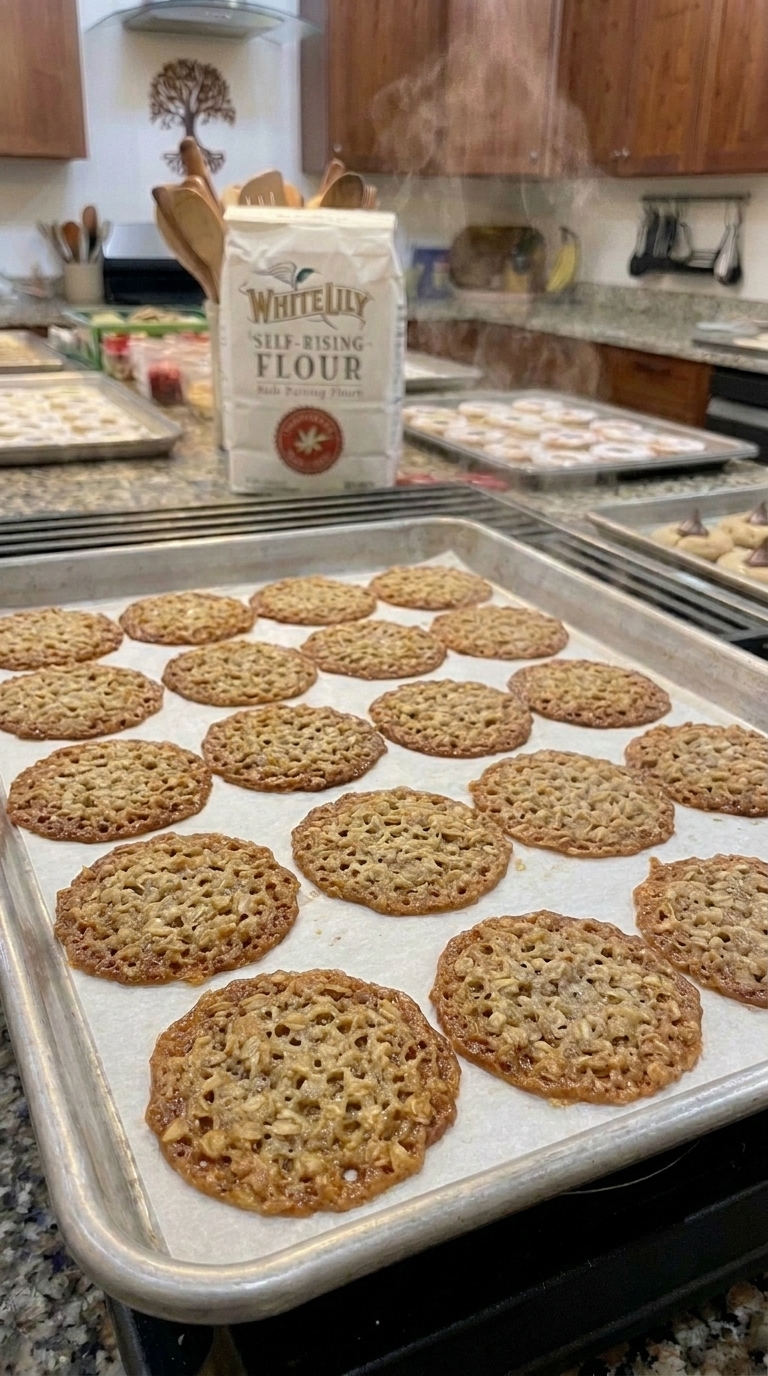 A stack of thin, golden-brown, lacy oatmeal cookies sitting on a cooling rack, catching the light to show their delicate web-like pattern.