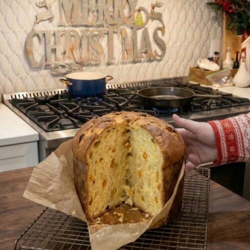 Homemade Italian panettone Christmas bread with a golden crust, raisins, and candied orange peel, baked in a tall paper mold.