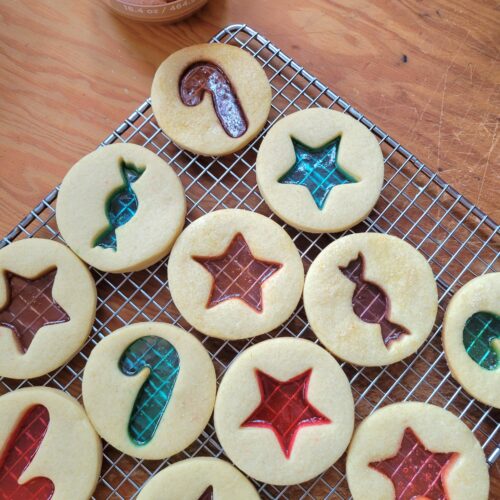 A silver baking tray filled with star-shaped sugar cookies featuring glowing, translucent red and green melted candy centers.