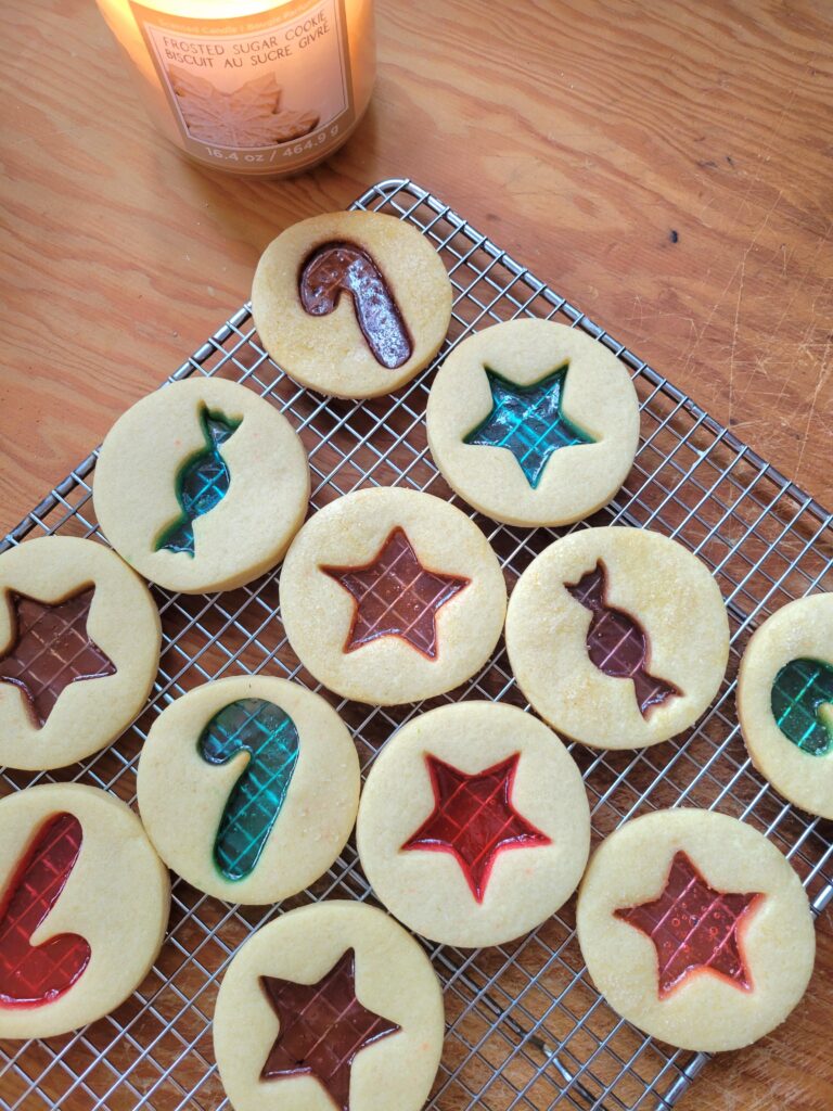 A silver baking tray filled with star-shaped sugar cookies featuring glowing, translucent red and green melted candy centers.