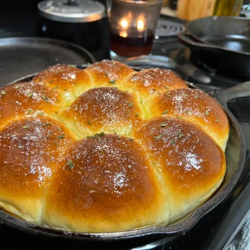 A well-seasoned cast iron skillet filled with eight golden brown, fluffy dinner rolls brushed with glistening herb butter.