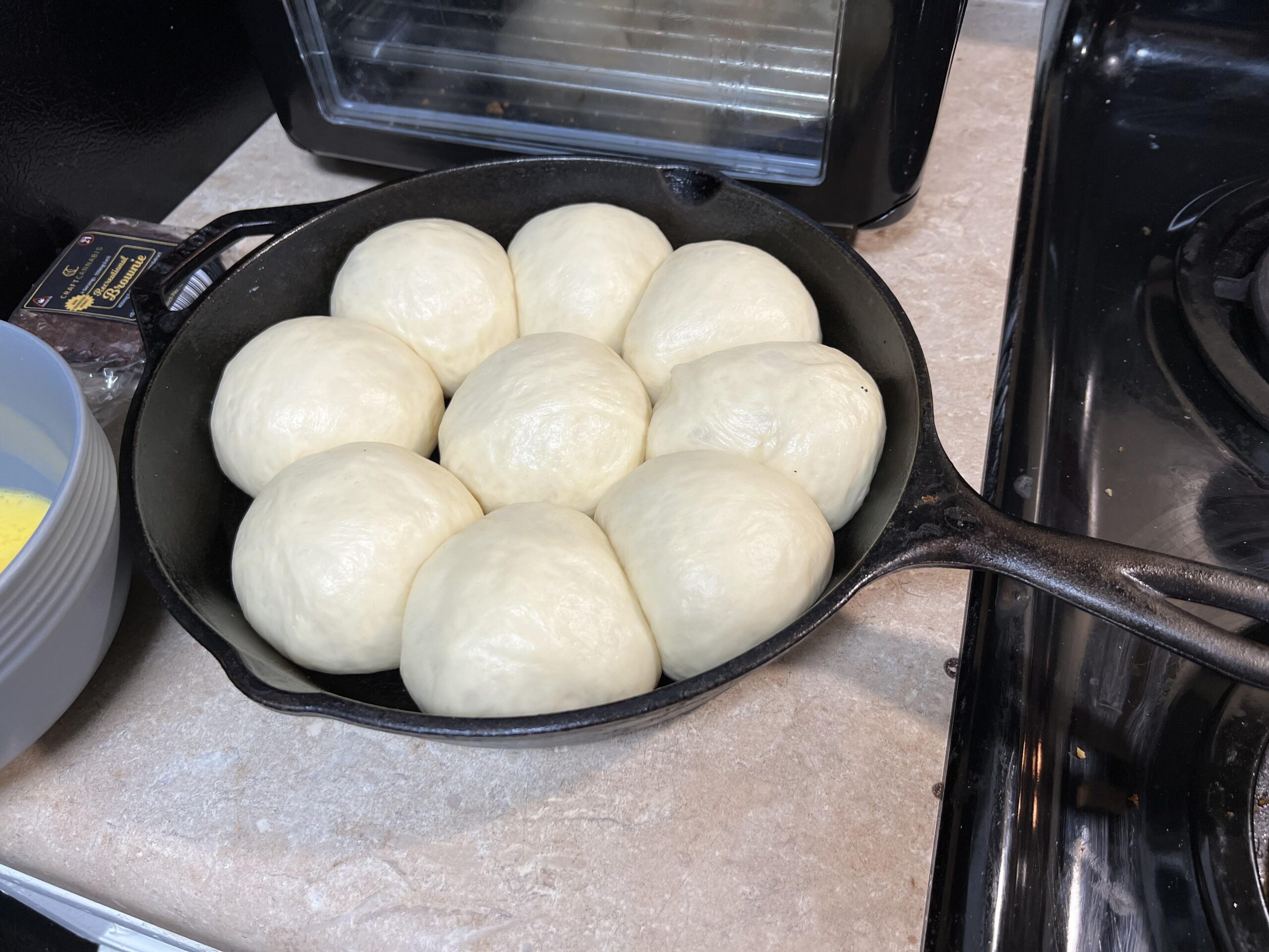 Eight perfectly smooth, round dough balls proofing inside a cast iron skillet on a kitchen counter, ready to be baked.