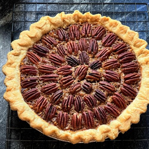 A delicious slice of classic Southern pecan pie resting on a speckled ceramic plate, showcasing a gooey, rich filling topped with perfectly baked pecan halves.