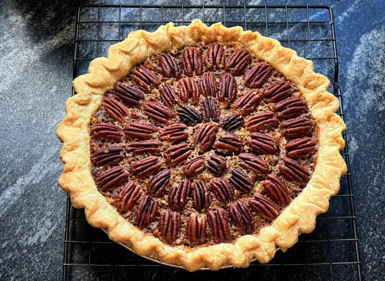 A delicious slice of classic Southern pecan pie resting on a speckled ceramic plate, showcasing a gooey, rich filling topped with perfectly baked pecan halves.