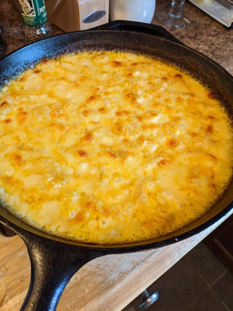 A bubbling cast iron skillet of baked macaroni and cheese with a golden-brown, crispy cheese crust on top.